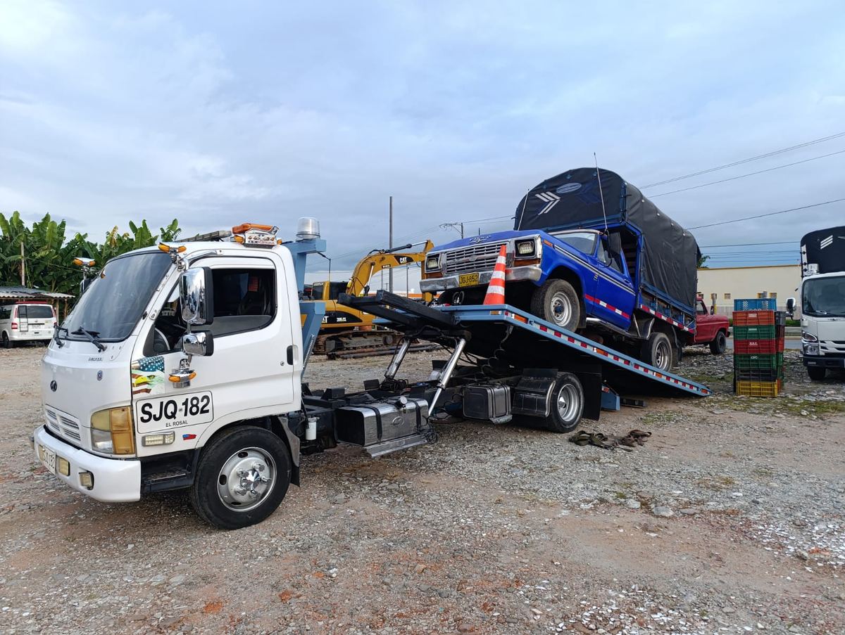 Camión de estacas Ford azul subiendo a la plataforma junto a maquinaria amarilla