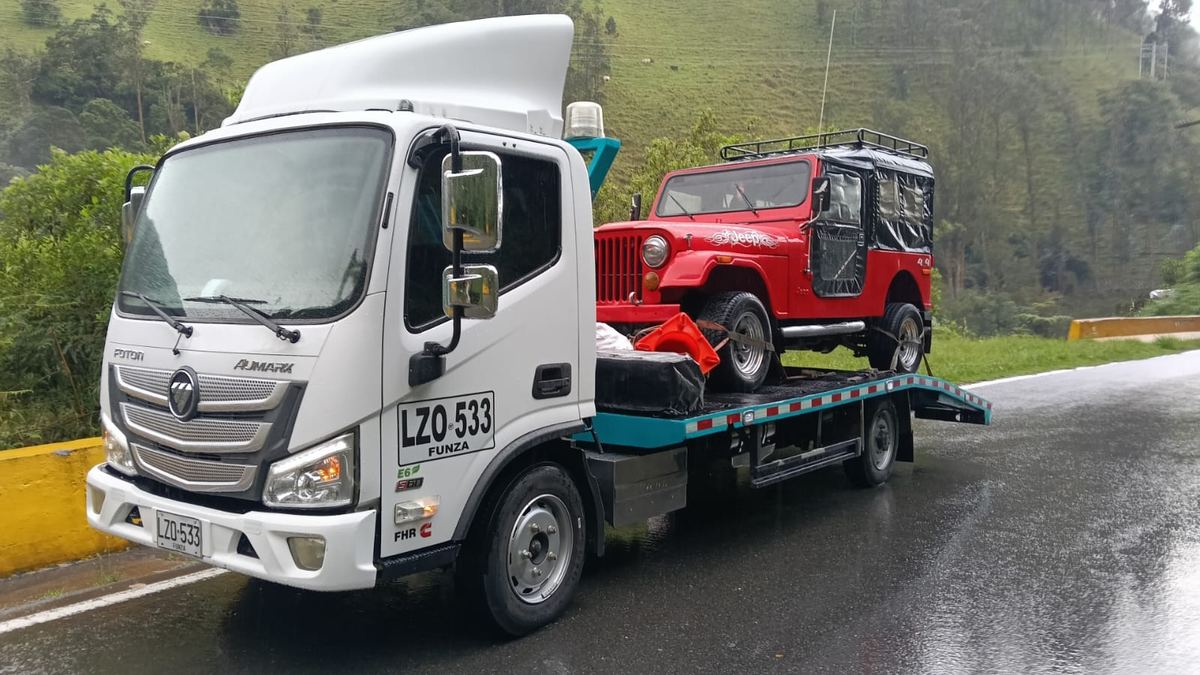Campero Jeep 4x4 rojo sobre la grúa de plataforma en una carretera de montaña del Quindío