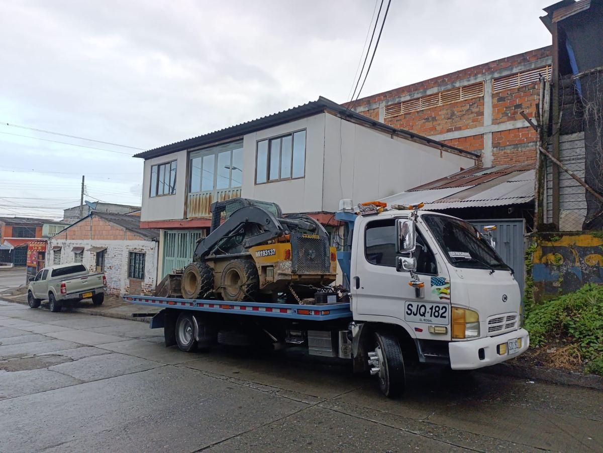 Grúa de plataforma cargando un minicargador en una calle de Armenia